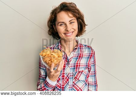 Young brunette woman holding bowl with italian pasta looking positive and happy standing and smiling with a confident smile showing teeth 