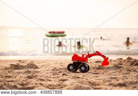 Toy Tractor On Sand Beach At Coast With Child Playing On Sea Blured. Sun Set On Ocean. Tourist In Tr