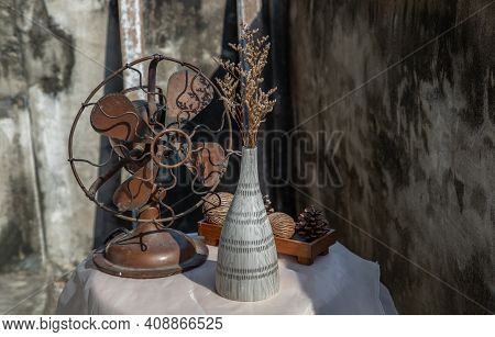 Dried Flowers In Ceramic Vase On Pink Textured Table Cloth And Vintage Fan With Old Cement Wall. Hom