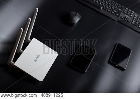 White Wifi Router, Branded Tenda With Smartphones And Keyboard From Pc, On Black Background.