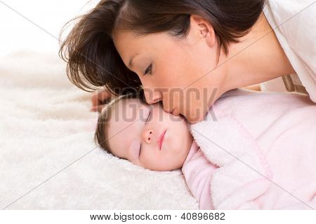 Baby pige og mor kysse hendes liggende glad på hvid pels tæppe