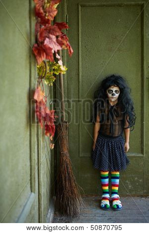 Portrait of Halloween girl with broom on background of wall of dilapidated house