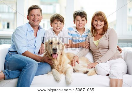 Cheerful family with their pet sitting on sofa at home