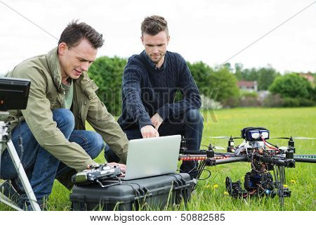 Young technicians using laptop by UAV drone in park