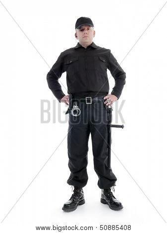 Security man wearing black uniform equipped with police club and handcuffs standing confidently with hands resting on hip , shot on white