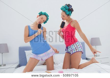 Girls in hair rollers singing with hairbrush in bed at sleepover