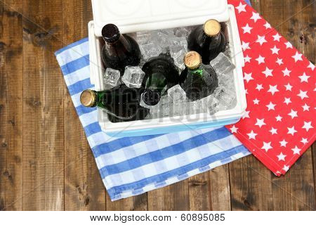 Ice chest full of drinks in bottles on color napkin, on wooden background