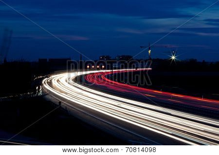 many cars are driving at night on a highway and create light trails.