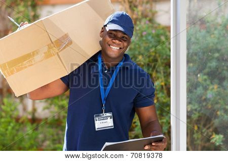 cheerful african courier standing with parcel at the door 
