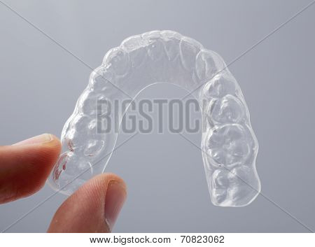 Hand holding a translucent essix retainer