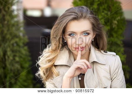 Young beautiful blonde woman has put forefinger to lips as sign of silence, outdoors