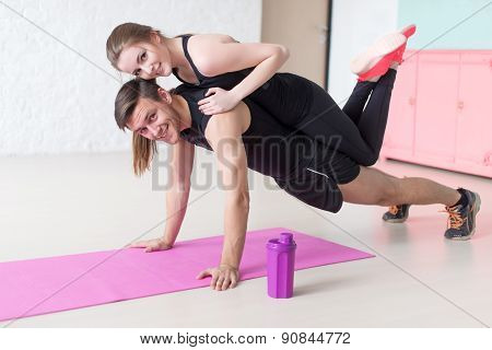 man doing push ups with woman laying on back at gym or home smiling looking camera concept fitness s