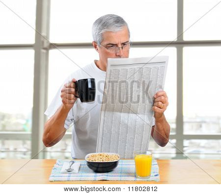 Medio di età uomo leggendo il giornale con prima colazione
