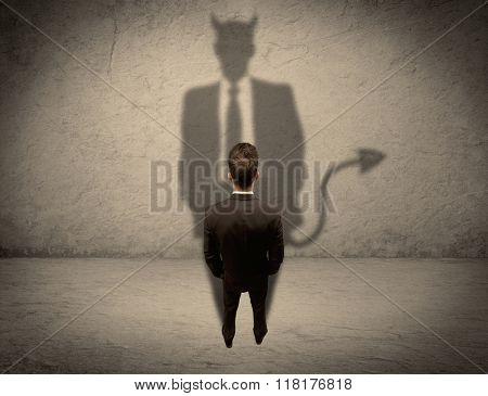 An experienced tricky businessman in suit looking at his devil desguise shadow reflected on the wall concept
