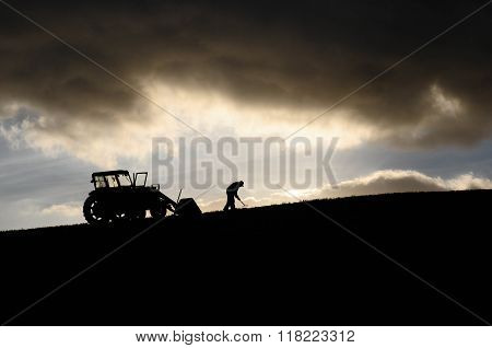 Silhouette of farmer working and tractor up high in the clouds
