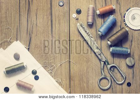 Sewing kit. Scissors, bobbins with thread and needles on the old wooden background