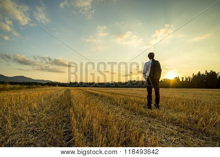 Businessman In Elegant Suit With His Jacket Hanging Over His Shoulder Standing In Mown Wheat Field