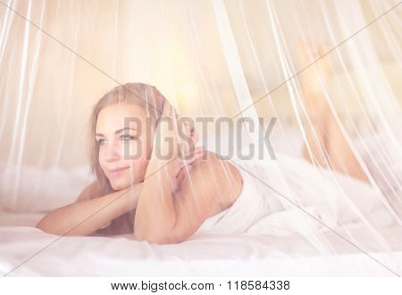 Portrait of cute dreamy woman in romantic bedroom, lying down on the bed with white tender net valance, spending holidays in spa hotel