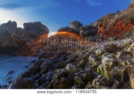 Man rotating fire on rocky shore