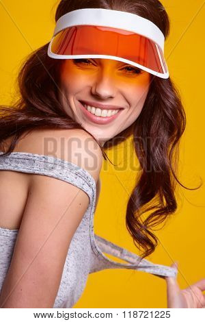 Smiling young woman in orange  sun visor posing in sunlight and looking away. studio shot on yellow background.