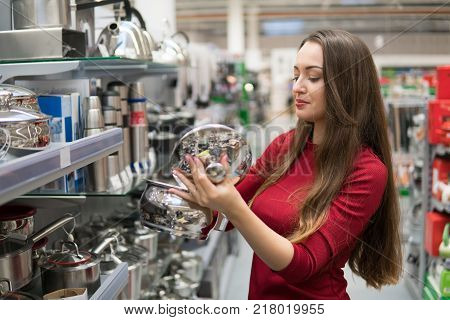 Smart housewife woman buys a saucepan in supermarket. Wide choice of kitchen utensils and cookware. she opened the lid of the pan