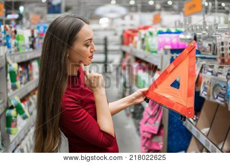 Closeup view of young female driver buys warning triangle in the supermarket car department. Safety shopping