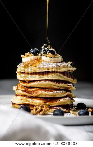 Pile of american pancake with blueberries. Maple leaf syrup is pouring  on it.