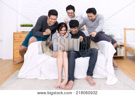 Group of five young asian people watching something with laptop and celebrate together at sofa in home or room. Happy and cheerful with friends in casual style. Funny and cheerful activity concpet.