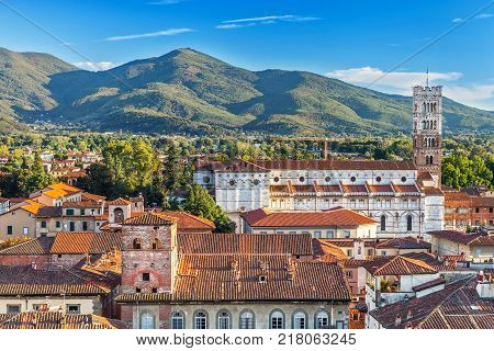 Vivid rooftops of city Lucca with background of colorful green mountains range Italy.