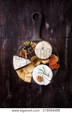 Cheese plate with blue cheese brie truffle hard cheese with grapes figs pears honey crackers dried fruits and nuts on dark table. Top view. Copy space.