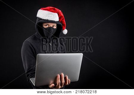 Mysterious male santa hacker holding laptop computer anonymous man on black background ransomware cyber attack and internet security on Christmas holiday concepts