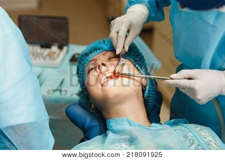 Male Old Professional Dentist Surgeon In Uniform And Female Assistant Helps To Performing Operation