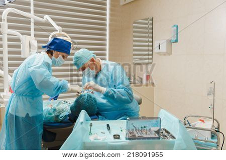 Male Old Professional Dentist Surgeon In Uniform And Female Assistant Helps To Performing Operation