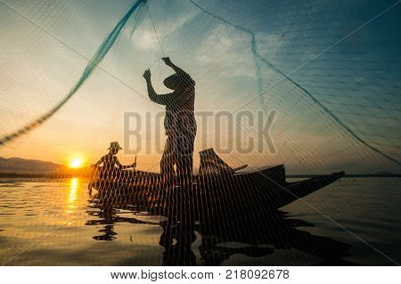 Asian Fisherman On Wooden Boat Casting A Net For Catching Freshwater Fish In Nature River In The Ear