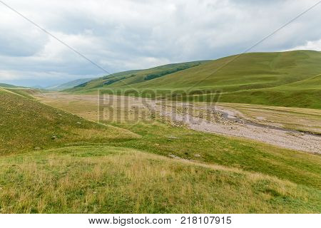 sheep near the bed of a mountain river, flock of sheep grazing in a hill on a green meadow, grazing sheep on the green hills of Assy Kazakhstan plateau.
