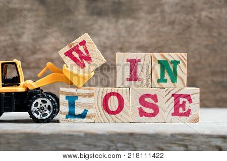 Yellow toy bulldozer hold letter block W to complete word win lose on wood background