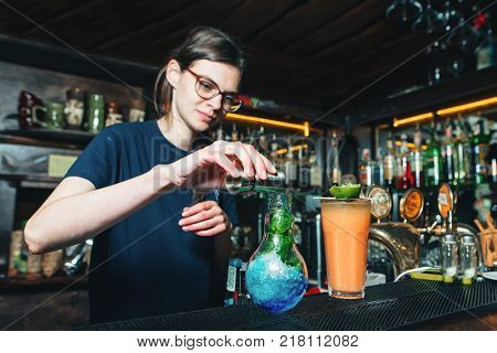 The bartender girl creates beautiful bright cocktails at the bar. The barman mixes the cocktail ingredients
