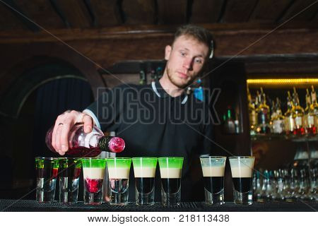 The barman creates alcoholic shots. The barman pours an alcohol in the glasses for the show