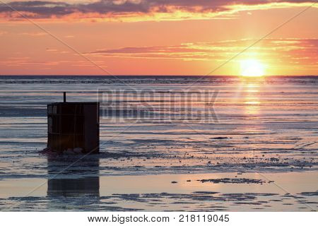 Ice fishing at sunset on a frozen harbour.