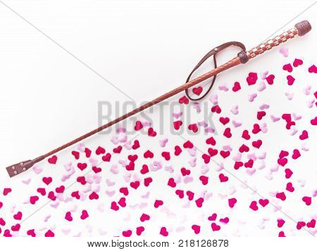 Brown leather whip are on a light background with pink and red heart made of cloth. Romantic background for goods from a sex shop, costume party, Valentine's Day