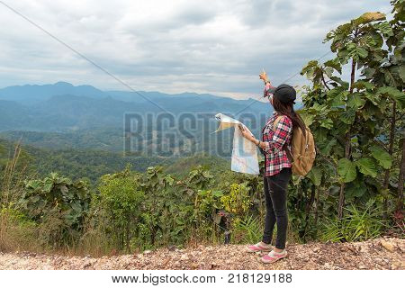 Asia woman traveler with backpack checks map to find directions in wilderness area explorer. Travel Concept.