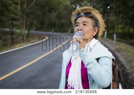 Happy hipster old women drinking water of bottle during backpack traveling on the road relax time in holiday color vintage style selective and soft focus