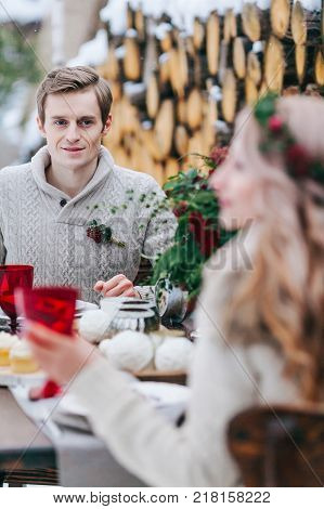 Handsome groom is tenderly looks at his beautiful bride throgh the table. Selective focus on the man. Winter wedding. Artwork