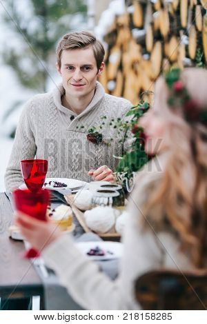Handsome groom is tenderly looks at his beautiful bride throgh the table. Selective focus on the man. Winter wedding. Artwork