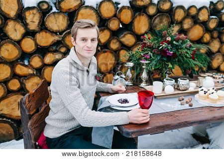 Handsome groom in warm cozy sweater sits at the festive decorated table. Winter wedding Artwork. Outdoors