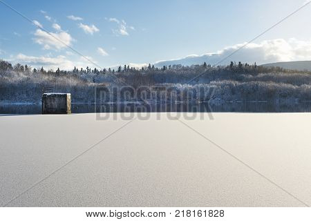 Winter landscape lake with a dam in the foreground against the forest and blue cloudy sky beautiful nature Western Ukraine