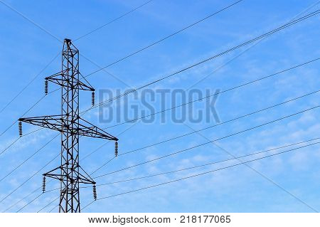 Metal support (elektroopora) of overhead power lines against a blue sky with clouds.