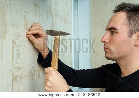 A Man Hammers A Nail Into Plaster Wall Under The Wallpaper