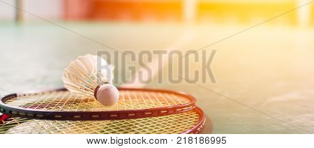 Badminton ball (shuttlecock) and racket on court floor banner panoramic crop for copy space. Badminton ball sunset. Badminton ball and racket. Badminton ball sunlight.