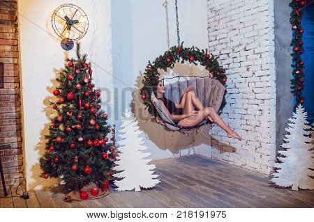 Woman in beautiful underwear sits in a hanging chair near Christmas tree. New year.